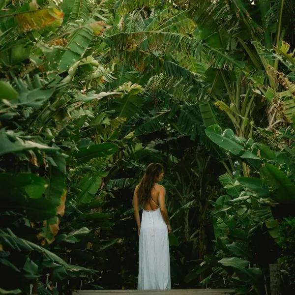 Mulher de vestido branco caminha por trilha entre bananeiras em Fernando de Noronha